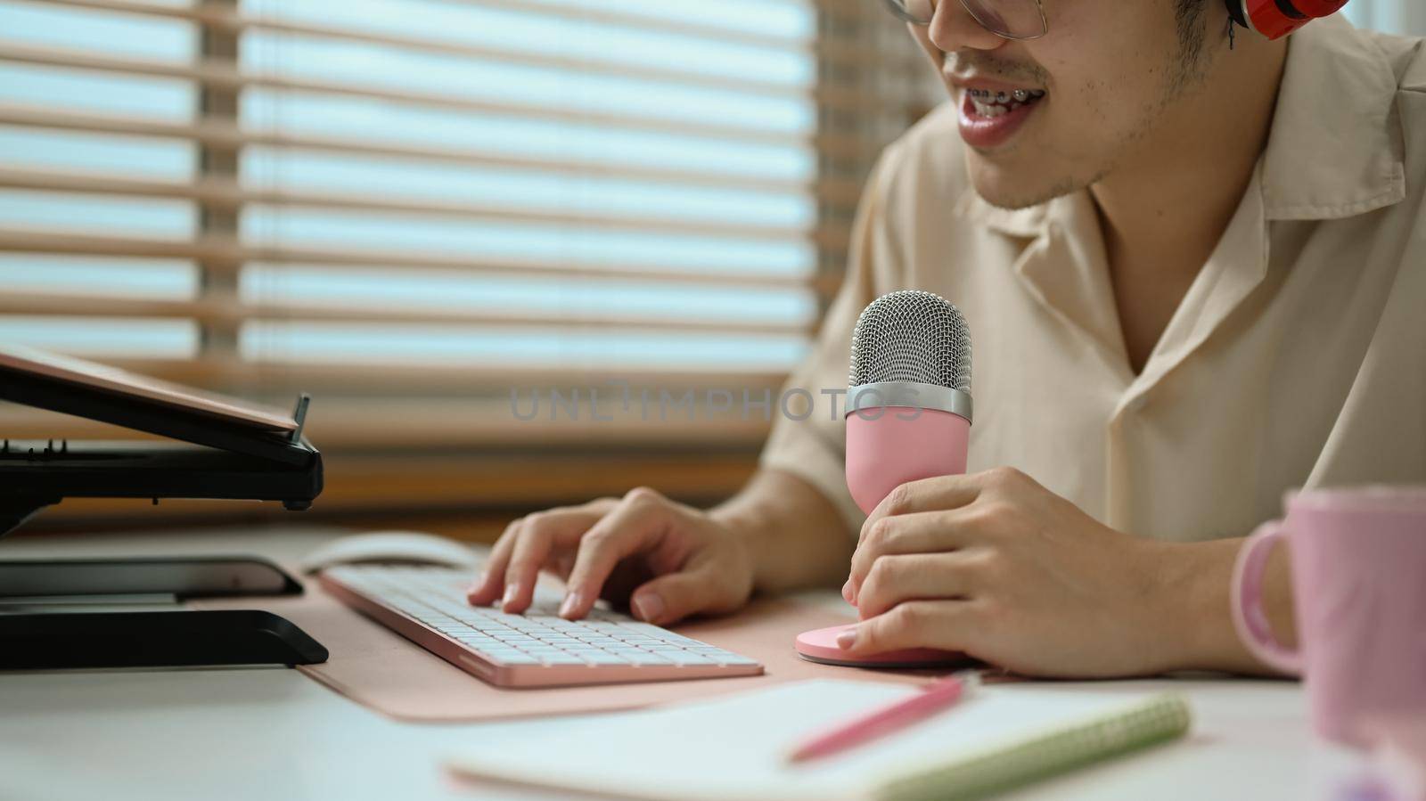 Young podcaster using a microphone and laptop computer recording audio for channel in home studio.