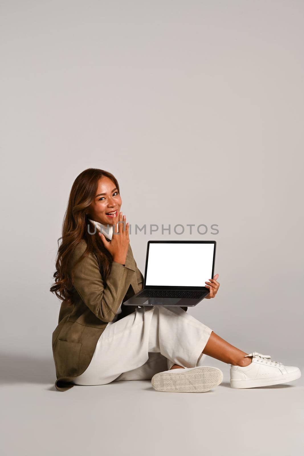 Image of attractive woman intrench coat sitting over white background and using laptop computer. People ans technology concept.