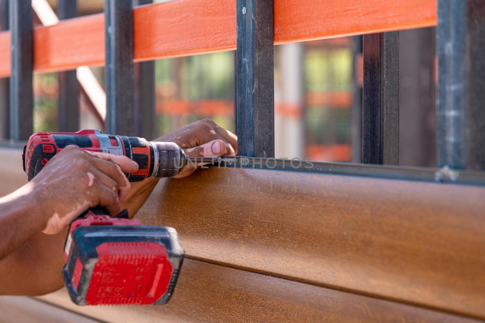 Man assembling composite wall siding using cordless screwdriver