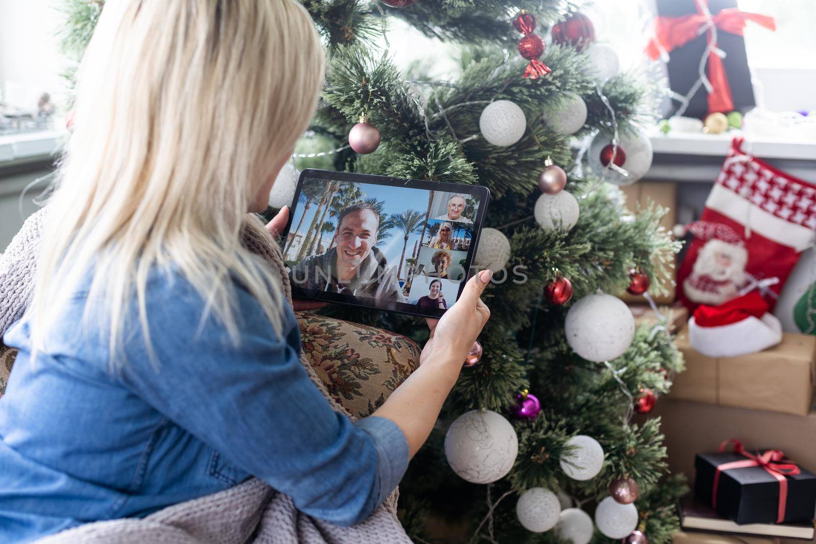 Christmas online holiday. Happy woman having video call with their family or friends. Young woman uses a digital tablet near decorated festive tree at home. Virtual meeting.