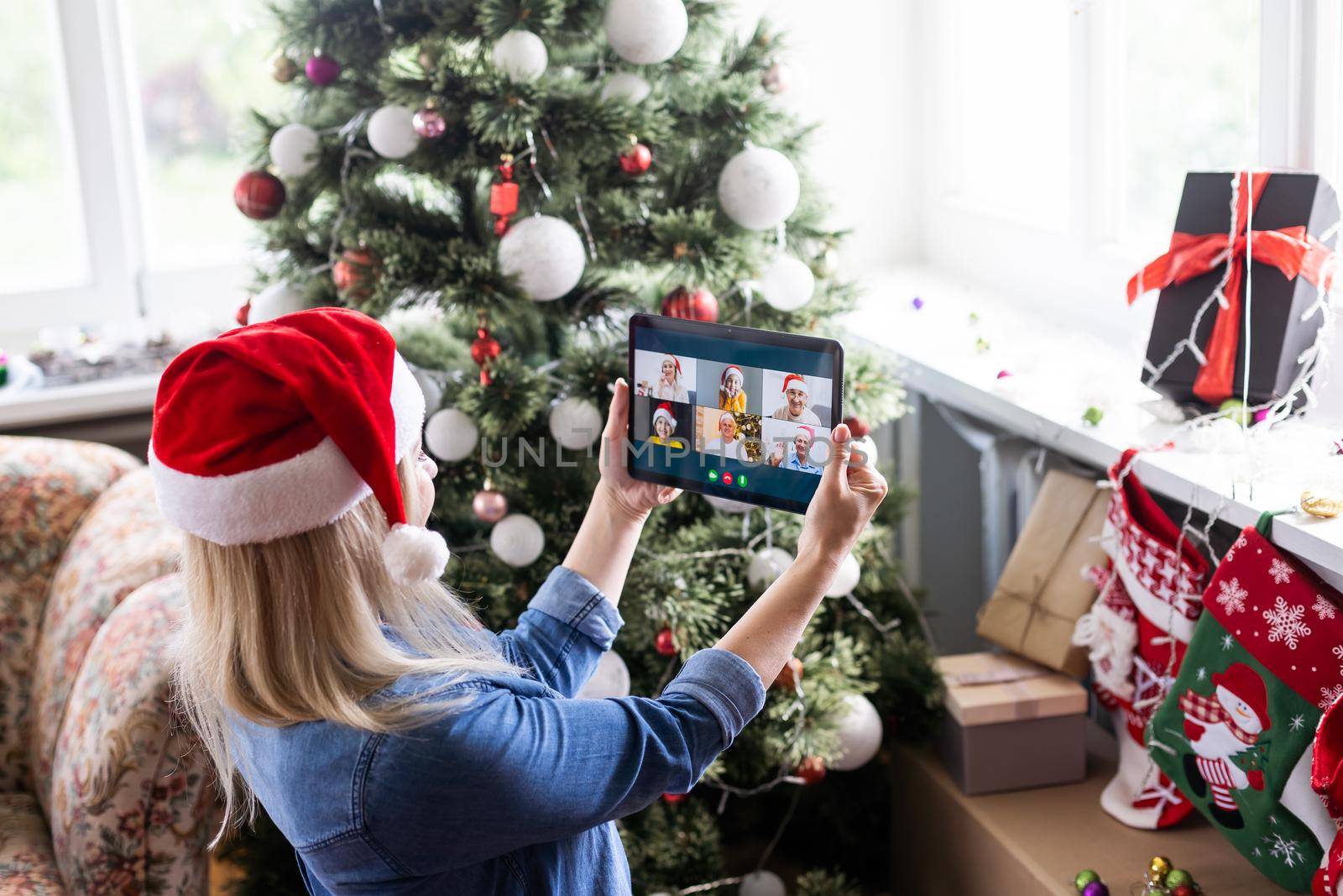 Woman with santa hat using video call conference on tablet, decorations and lights at home. Caucasian adult for christmas eve party.