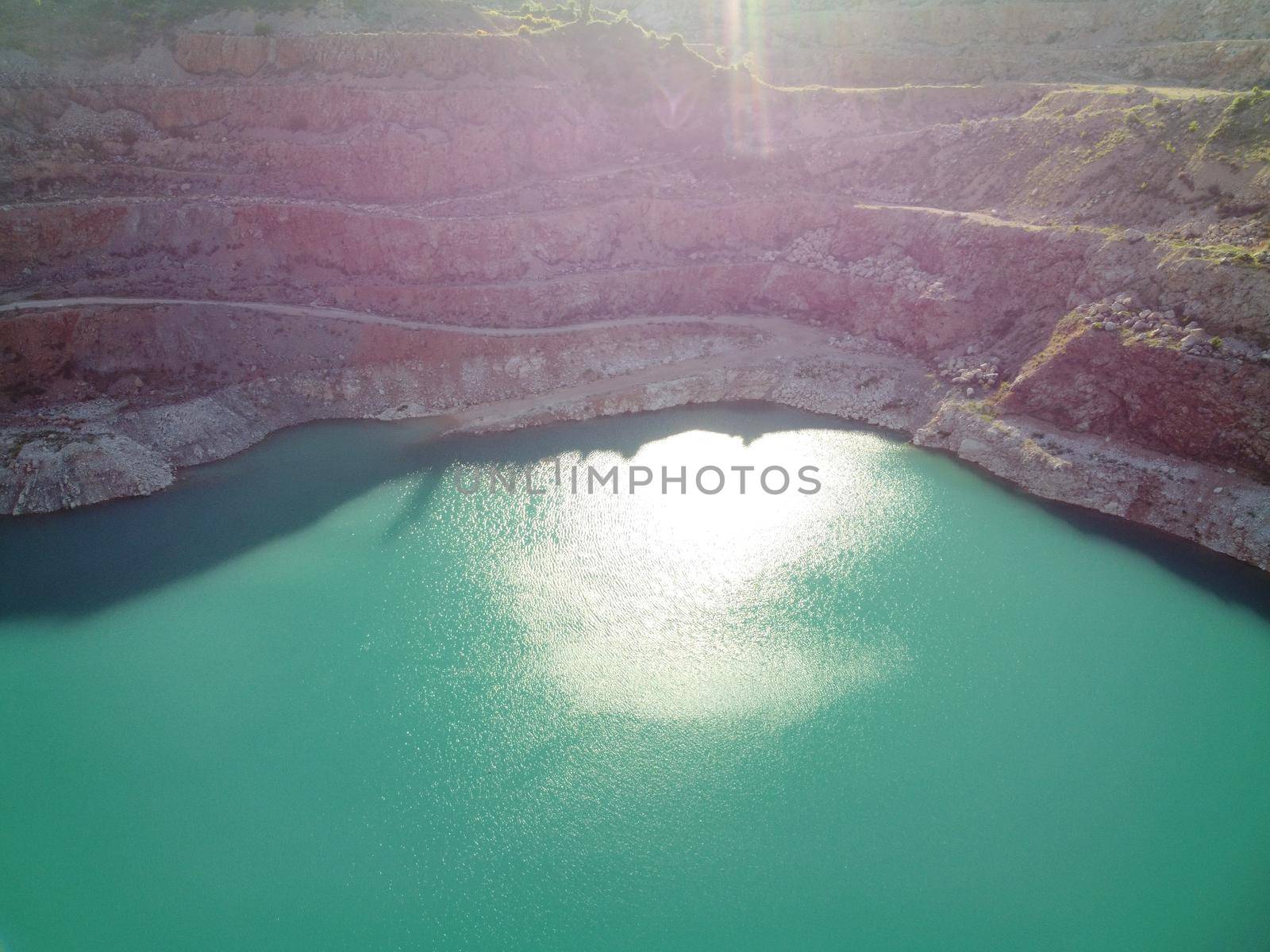 Flight over the turquoise surface of the lake in the center of the quarry. Industrial of opencast mining quarry with flooded bottom. Small lake in the shape of a heart
