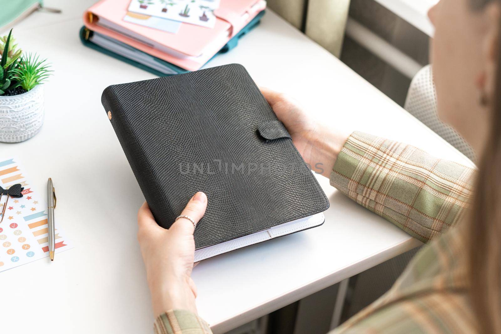 Close up picture of woman hands holding black mockup notebook. Girl holding a black blank space notepad with small cactus on the table. Mockup blank copy space notepad.