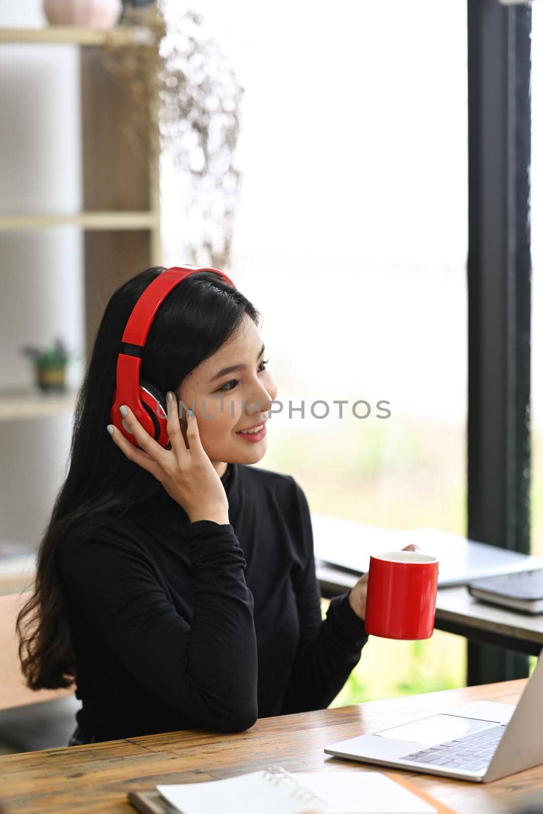 Happy young woman listening to music in headphone and drinking hot beverage.