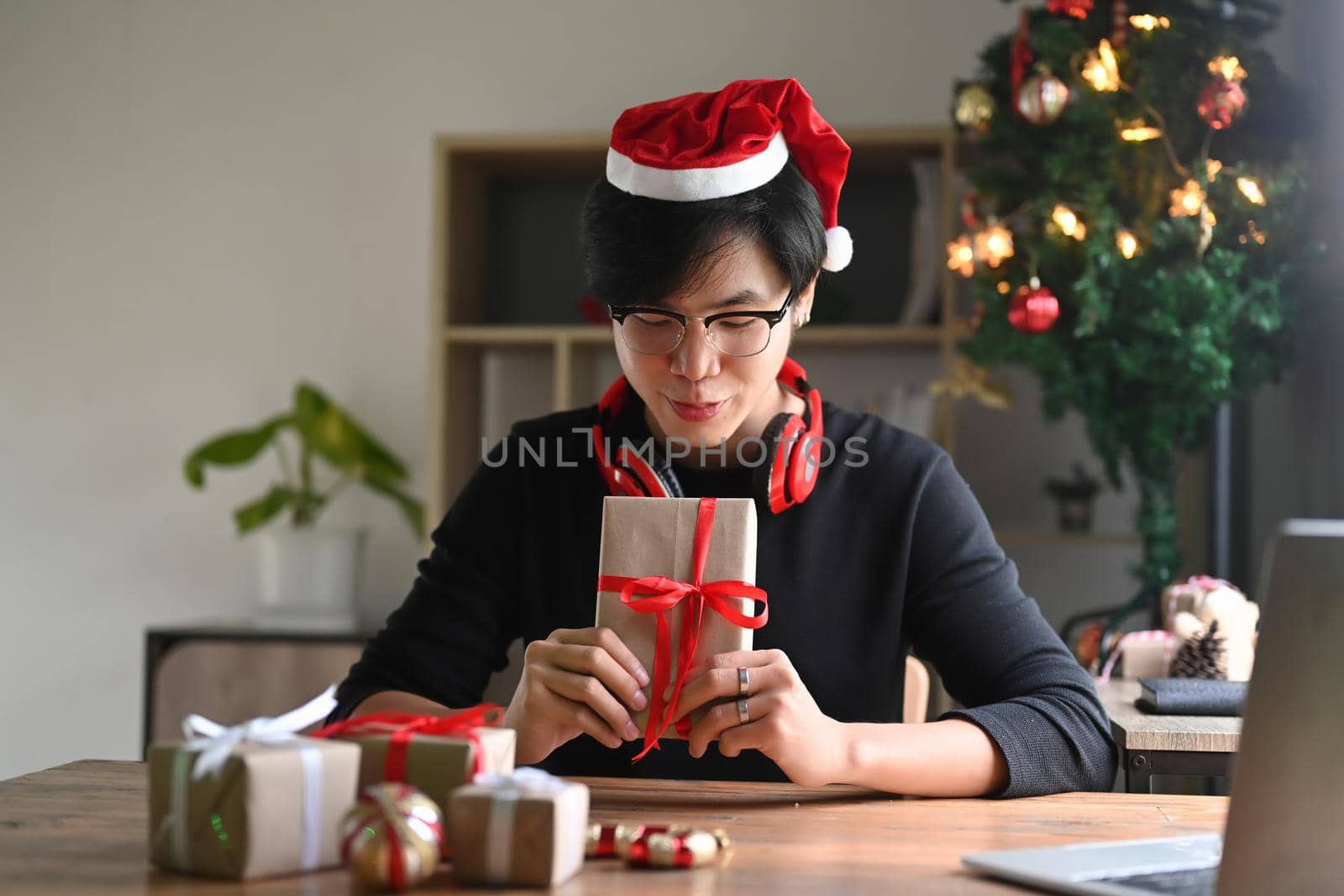 Young man in Santa hat holding Christmas presents with red ribbon.