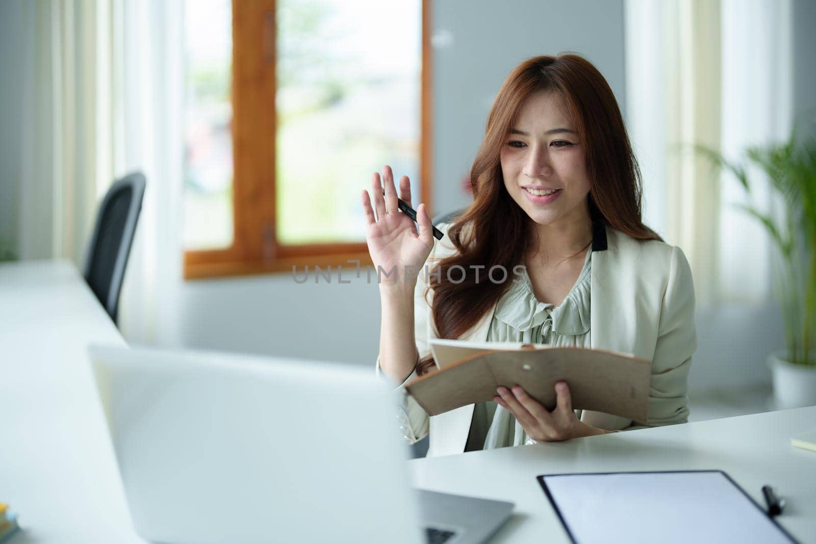 Portrait of an Asian bank employee using a laptop video conferencing with team members working on budget paperwork at their desk in their office.