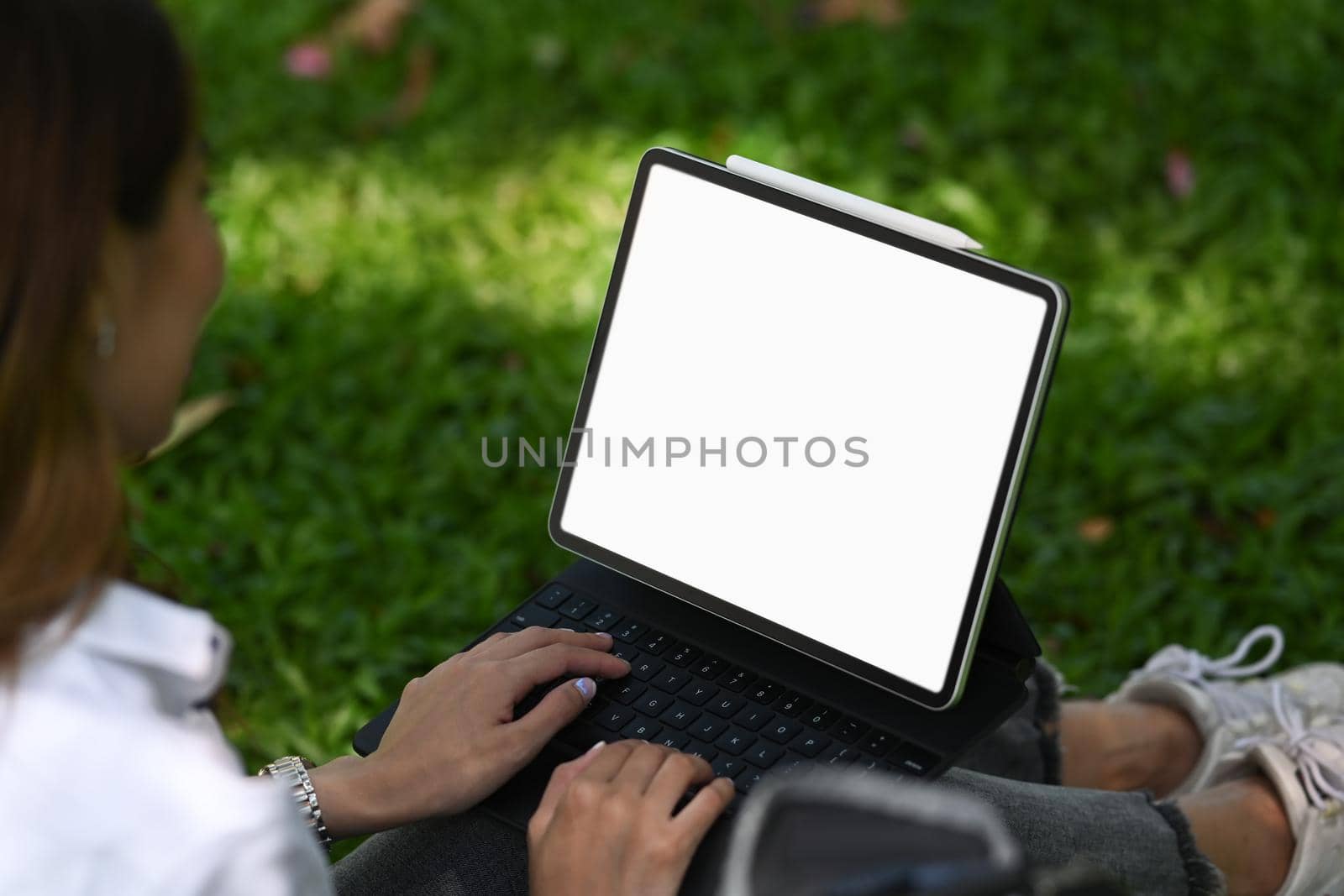 Young woman sitting on green grass in the nature park and working with digital tablet.