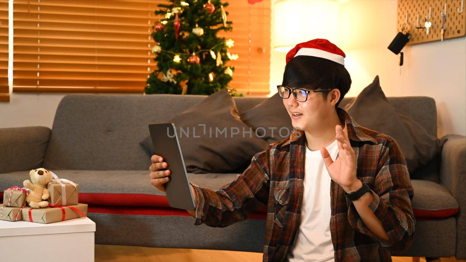 Smiling Asian man having video call with family on digital tablet in living room.