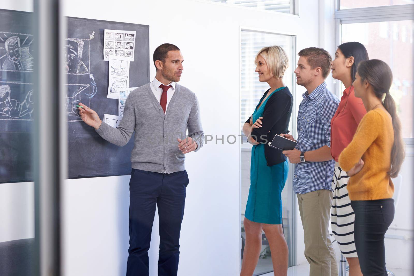 Communication is the brother of leadership. A businessman standing and presenting a storyboard to his team in an office. by YuriArcurs