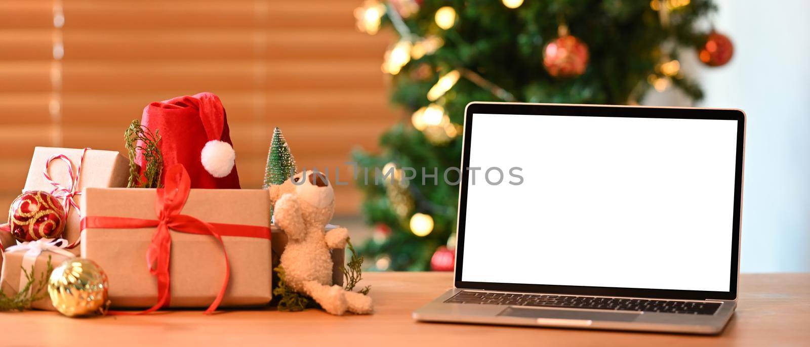 Mock up laptop computer and Christmas gift boxes on wooden table.