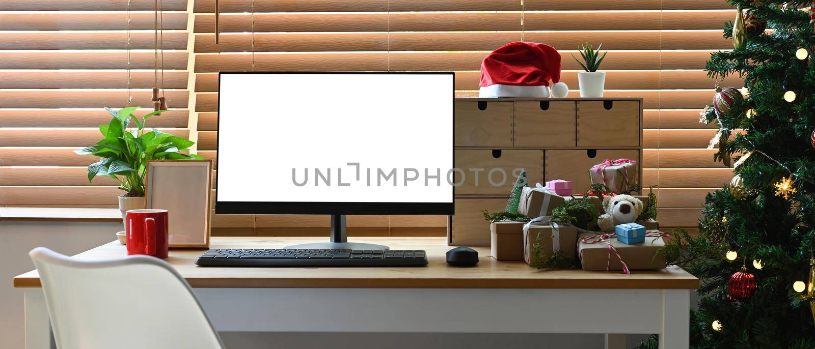 Mock up computer with white display, houseplant and Christmas gifts on wooden table.