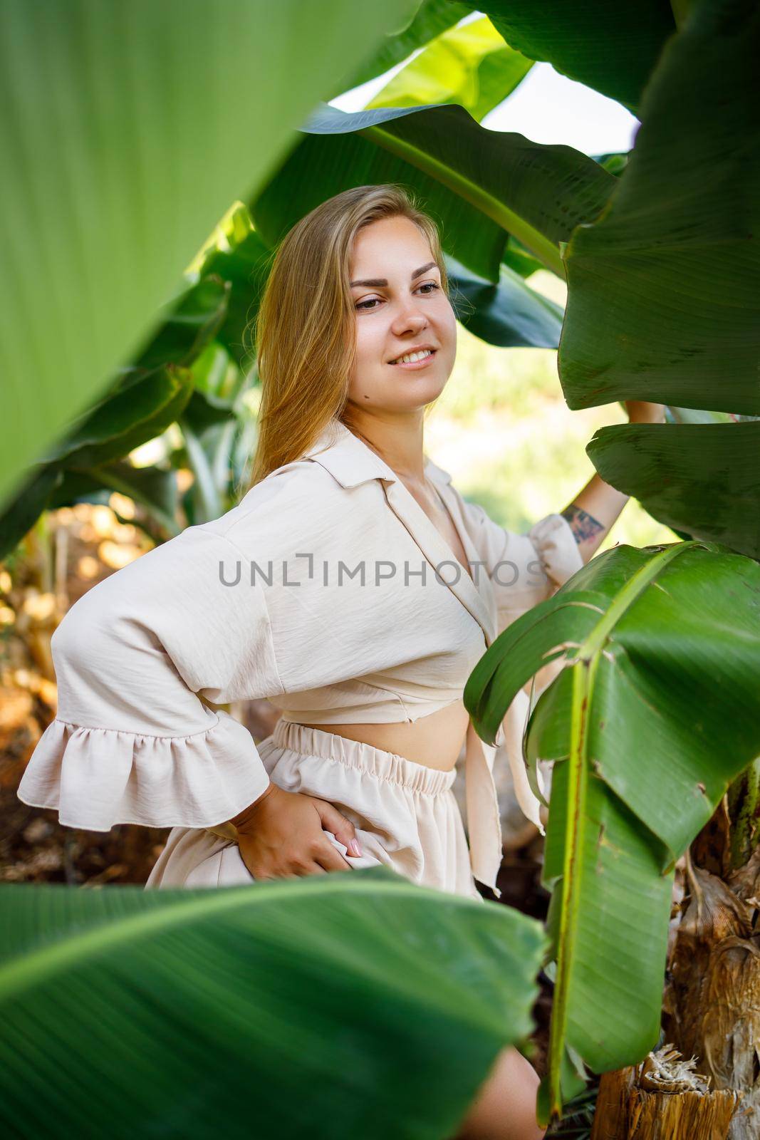 Woman near green leaves of banana bushes on nature in a park in a tropical place, she is in a beige skirt and a blouse