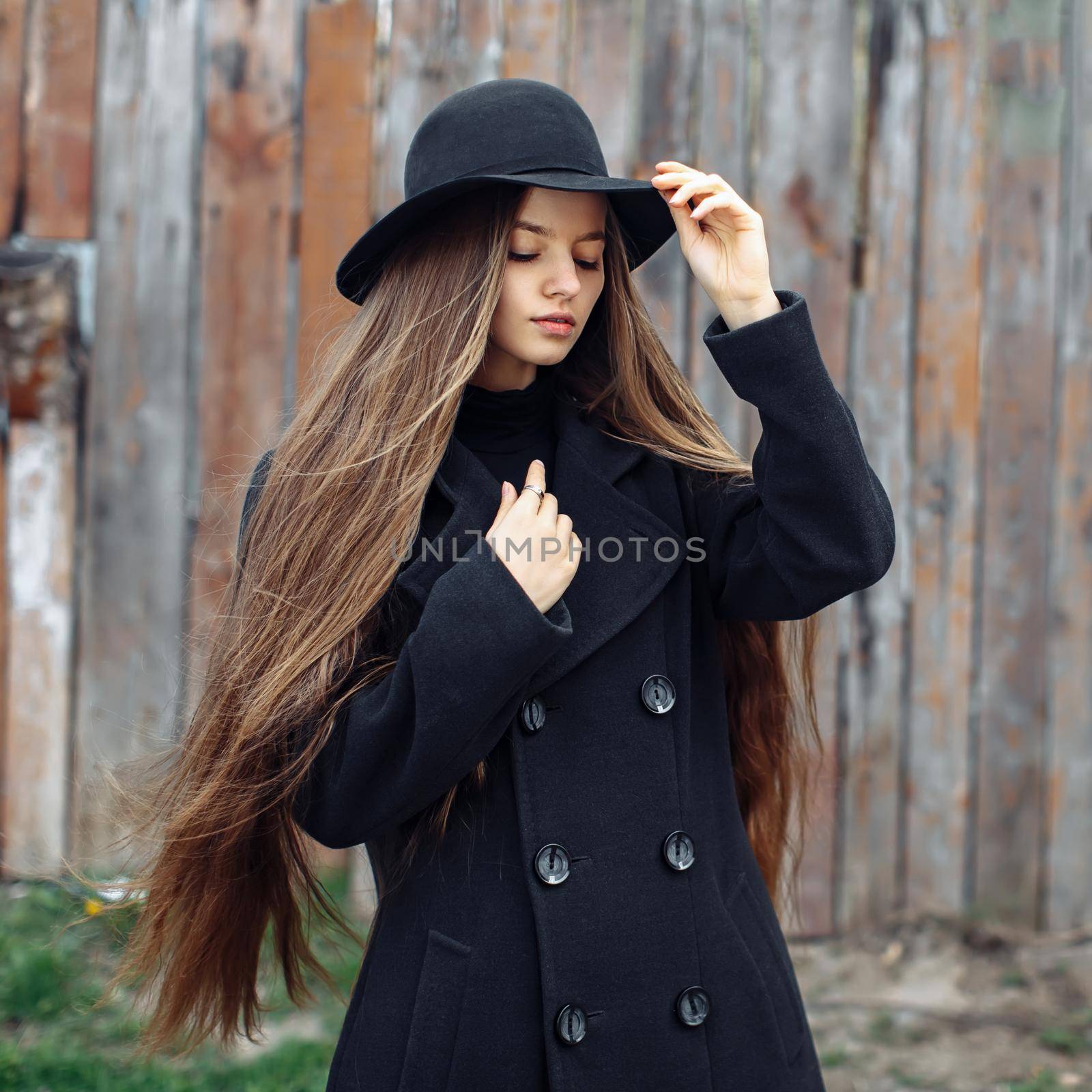 Young beautiful fashionable woman in black hat, with long hair posing on woody background. Female fashion, beauty concept. Outdoor.