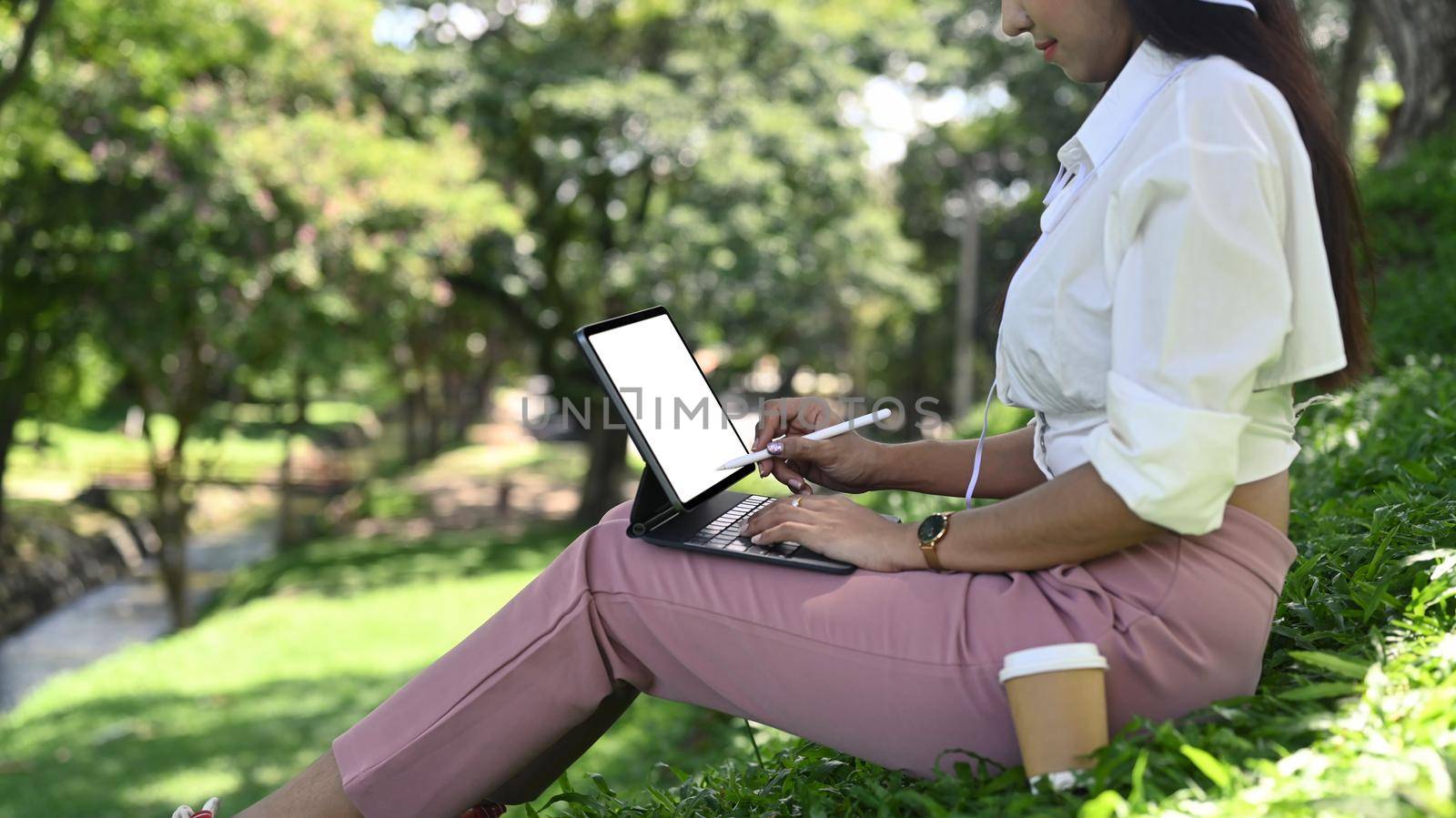 Young woman sitting in public park and working with computer tablet.