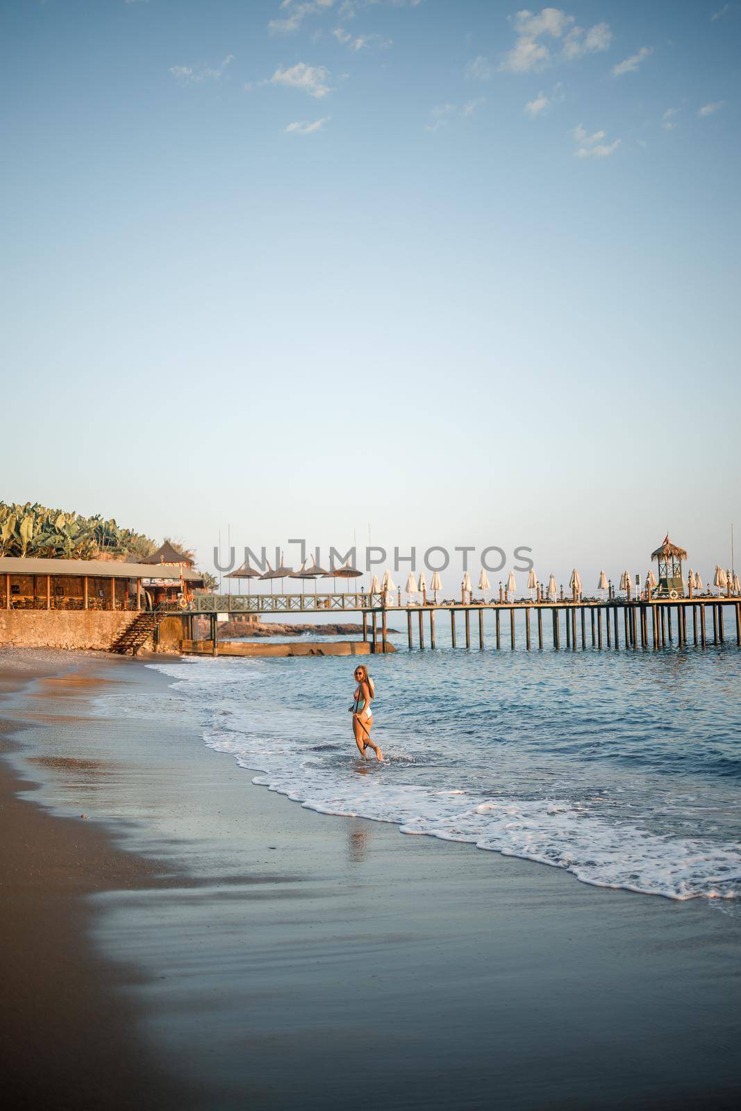 A woman in a swimsuit and a hat with glasses walks along the beach at sunset. The concept of sea recreation. Selective focus