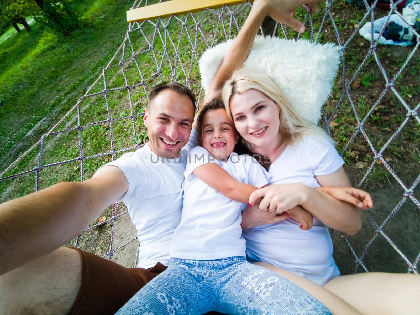 family laying down and relaxing together on a hammock during a sunny summer day on holiday home garden. Family relaxing outdoors, healthy and wellness lifestyle. by Andelov13