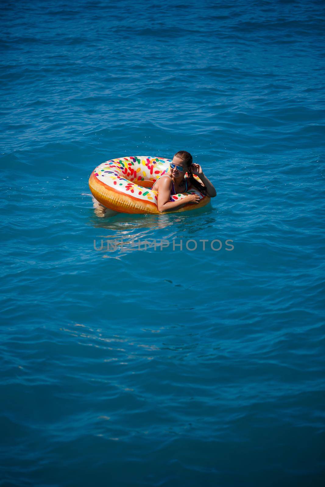 Beautiful young woman in the sea swims on an inflatable ring and has fun on vacation. Girl in a bright swimsuit at the sea under the sunlight