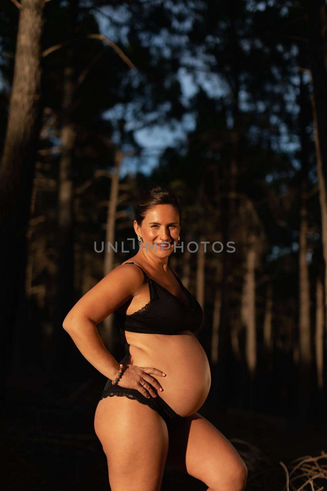 A pregnant woman caresses her belly and smiles at camera wearing black underwear by stockrojoverdeyazul