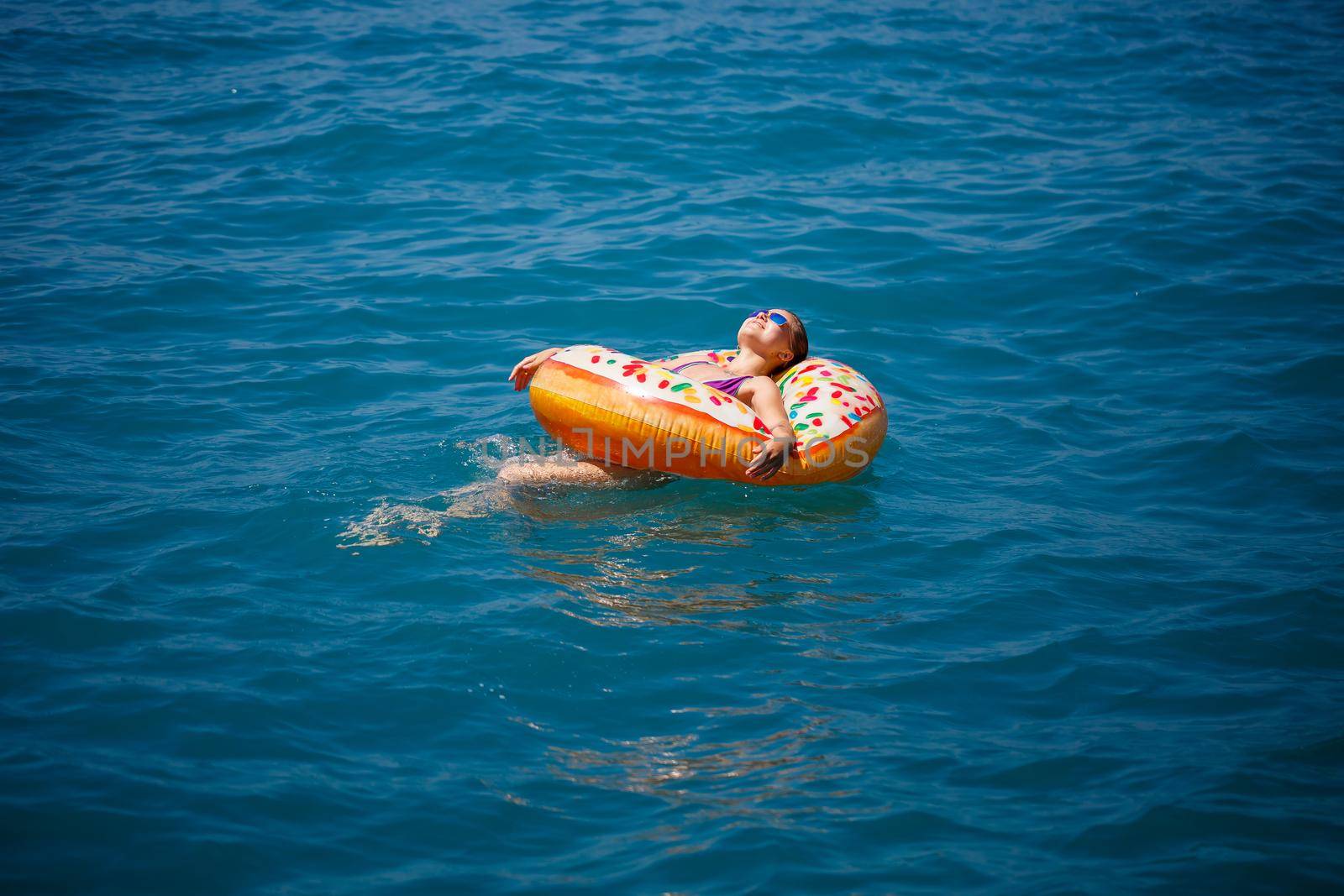 Beautiful happy young woman in a swimsuit with an inflatable ring relaxing in the blue sea. Sunny day, seaside vacation, tourism