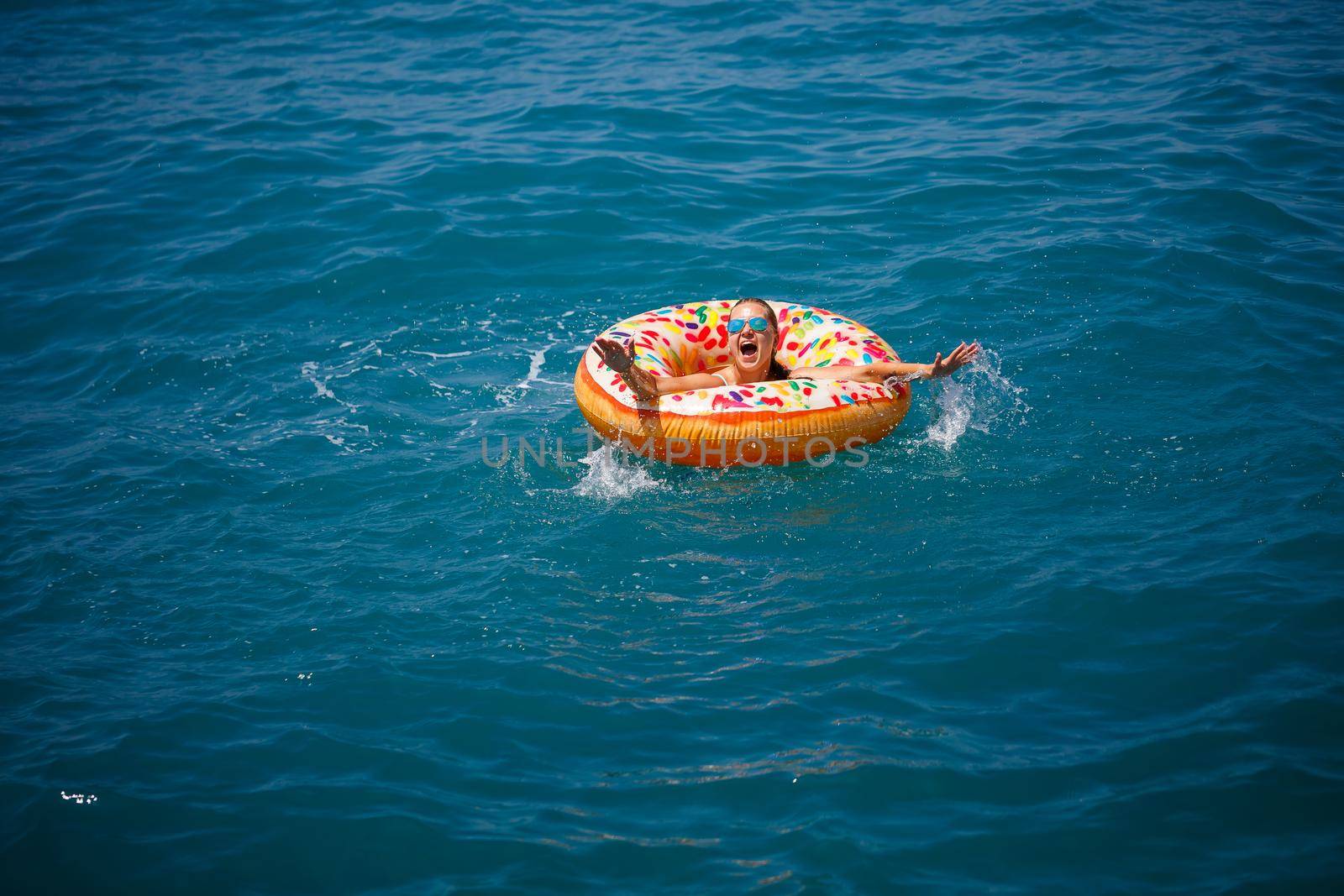 Young woman floating on an inflatable big donut in the transparent turquoise sea. View of a slender lady relaxing on vacation in Turkey, Egypt, Mediterranean Sea.