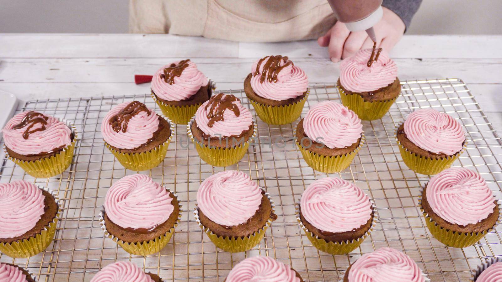 Drizzling chocolate ganache on top of bake chocolate raspberry cupcakes.