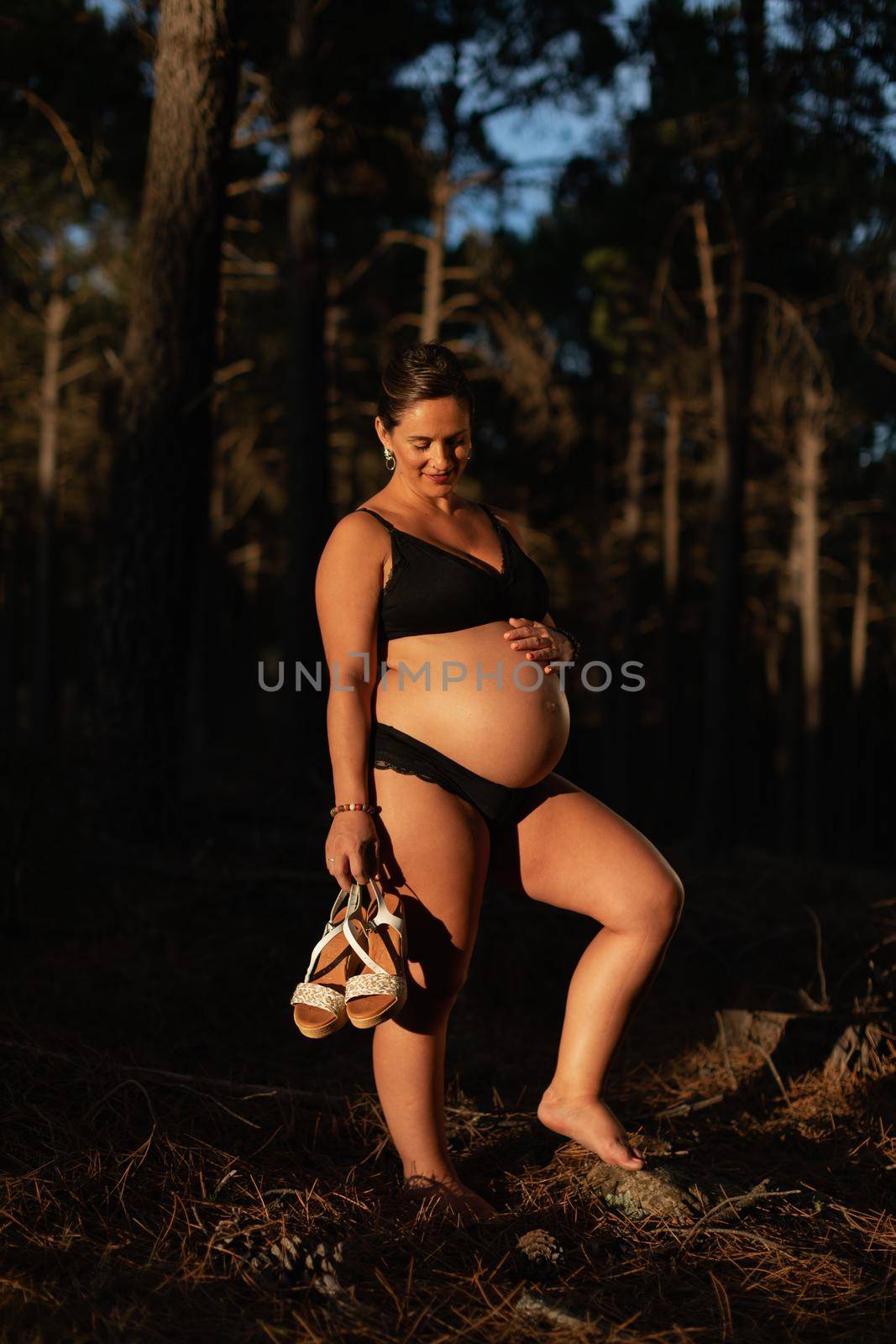 A pregnant woman caresses her belly and smiles while holing her shoes by stockrojoverdeyazul