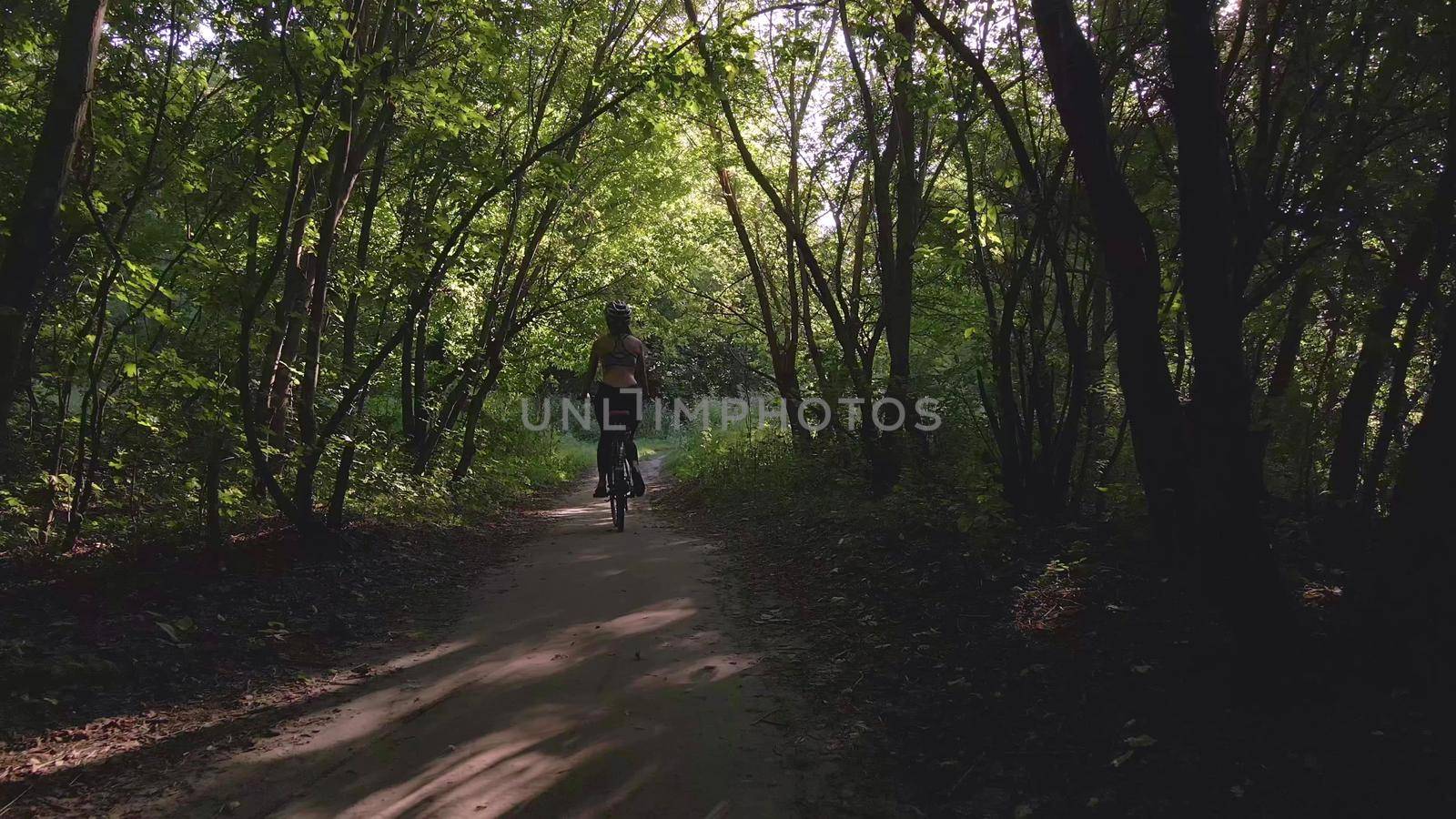 Aerial shot of young sexy sport woman rides bicycle on forest road at summer sunset. Happy holiday or workout on sunny summer day. Healthy cycling lifestyle. 4k slow motion 60 fps