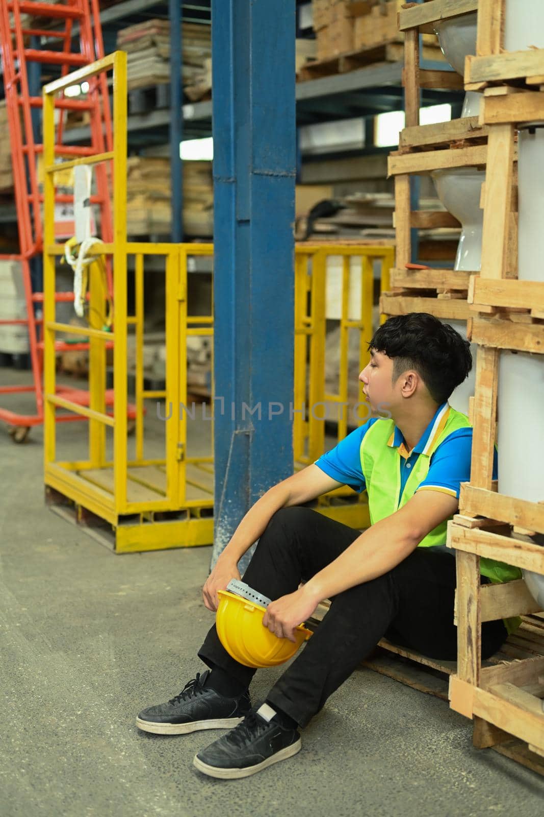 Warehouse workers in safety uniform working in warehouse full of tall shelves with goods in cardboard boxes by prathanchorruangsak