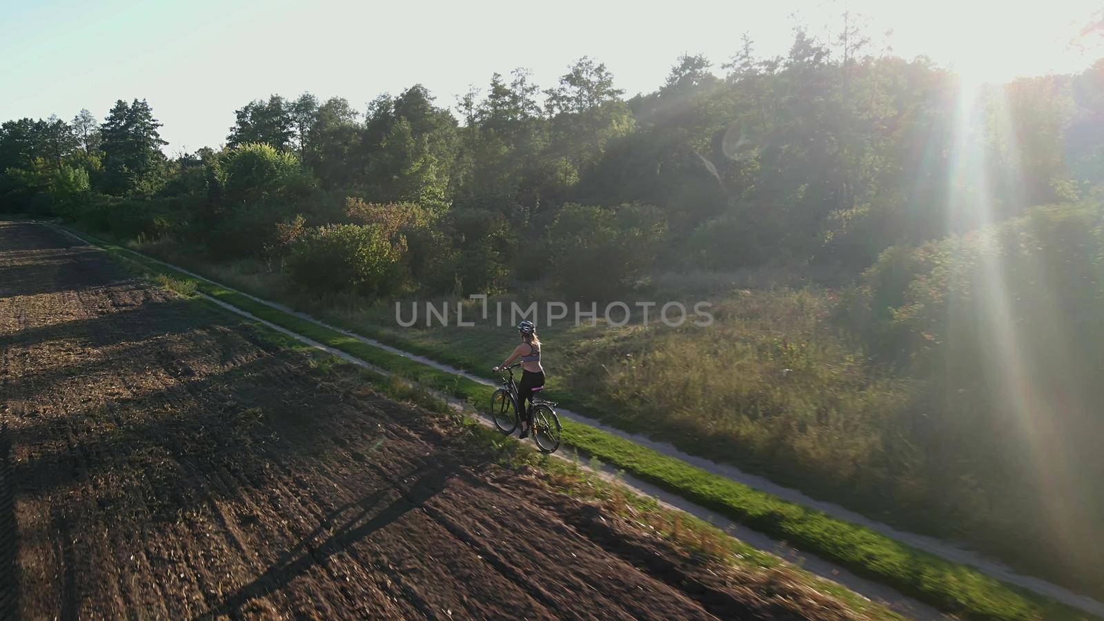 Aerial shot of young sexy sport woman rides bicycle on countryside road at summer sunset. Happy holiday or workout on sunny summer day. Healthy cycling lifestyle. 4k