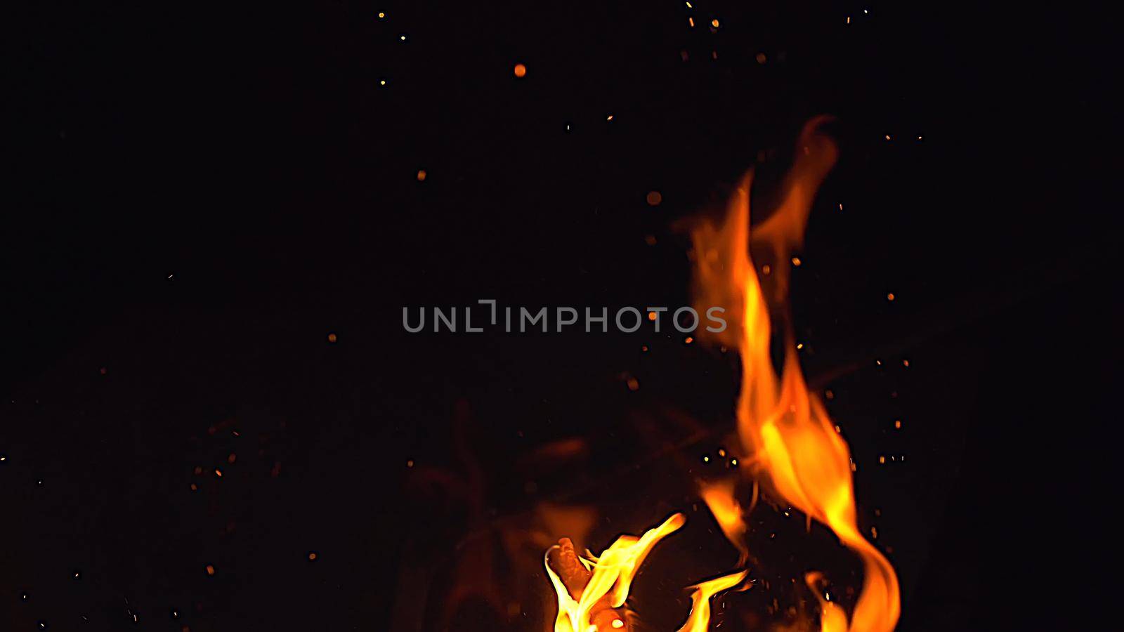 Fire flames and a lot of bright sparks are flying from the fire at black background