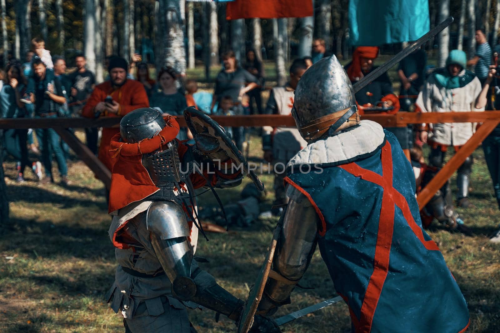 Two warriors in medieval costumes and with shields fight with swords. Reconstruction of historical jousting tournaments. Festival of medieval culture in park. Bishkek, Kyrgyzstan - October 13, 2019