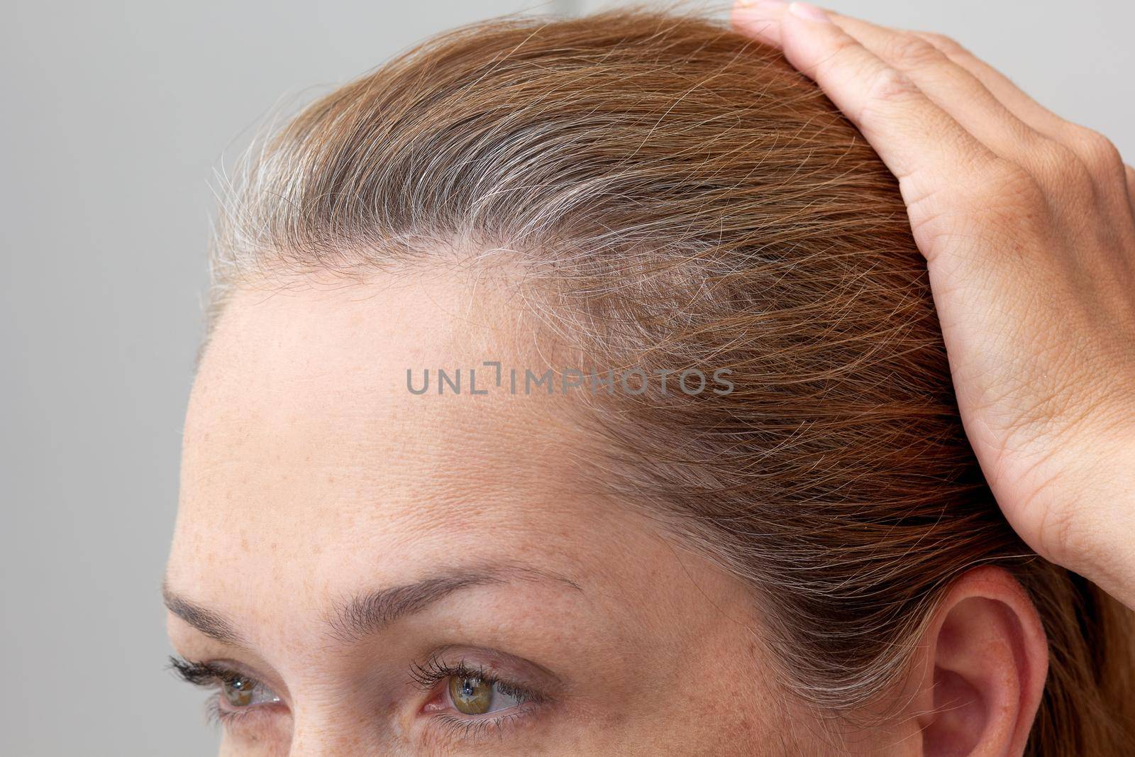 Cropped face of woman holding hand on head showing grey hair