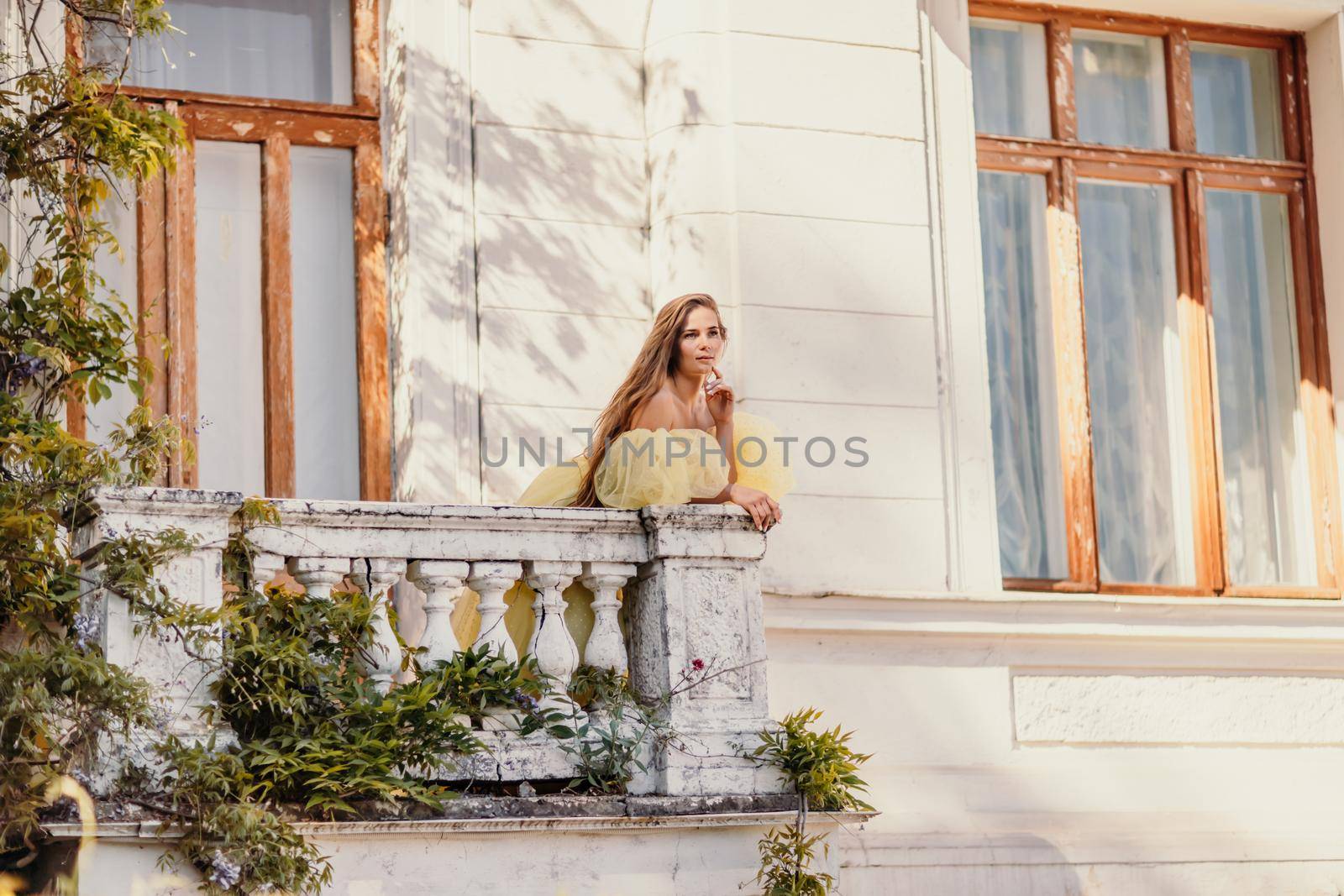 a beautiful smiling and kind woman in a gorgeous yellow dress stands on the balcony of an old vintage house by Matiunina