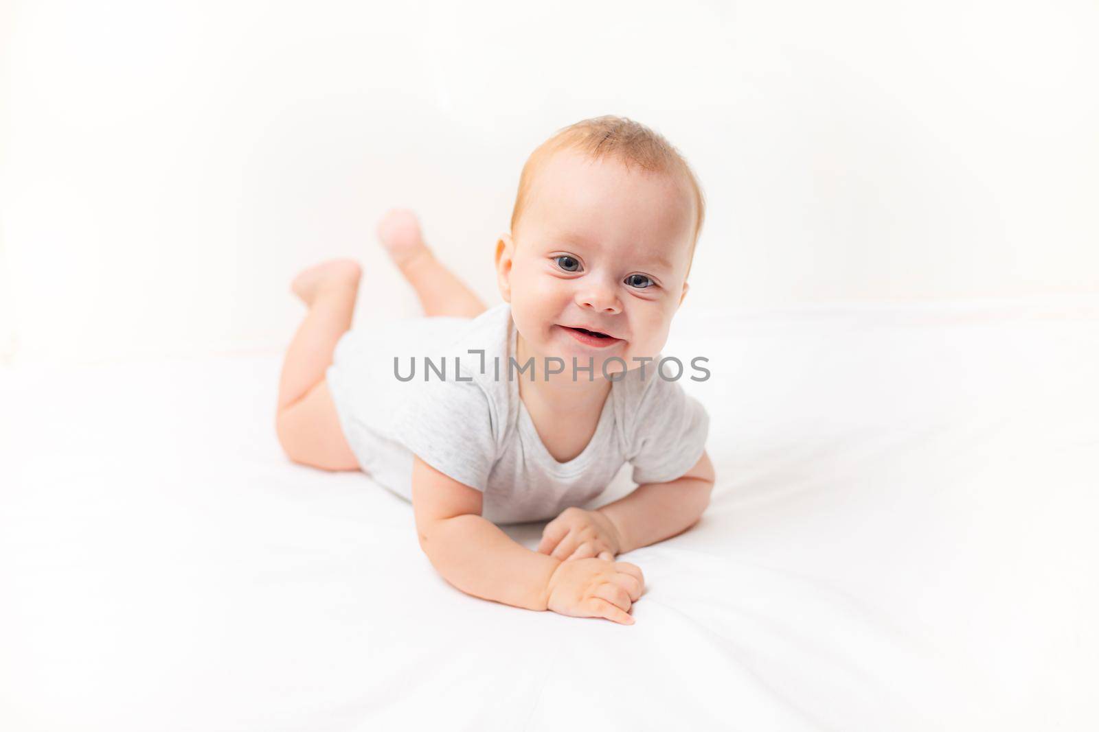 The baby lies on a white background and smiles at the camera . Advertising of children's goods. A child on a white background. Happy baby. The smile of a child. Children 's article . by alenka2194