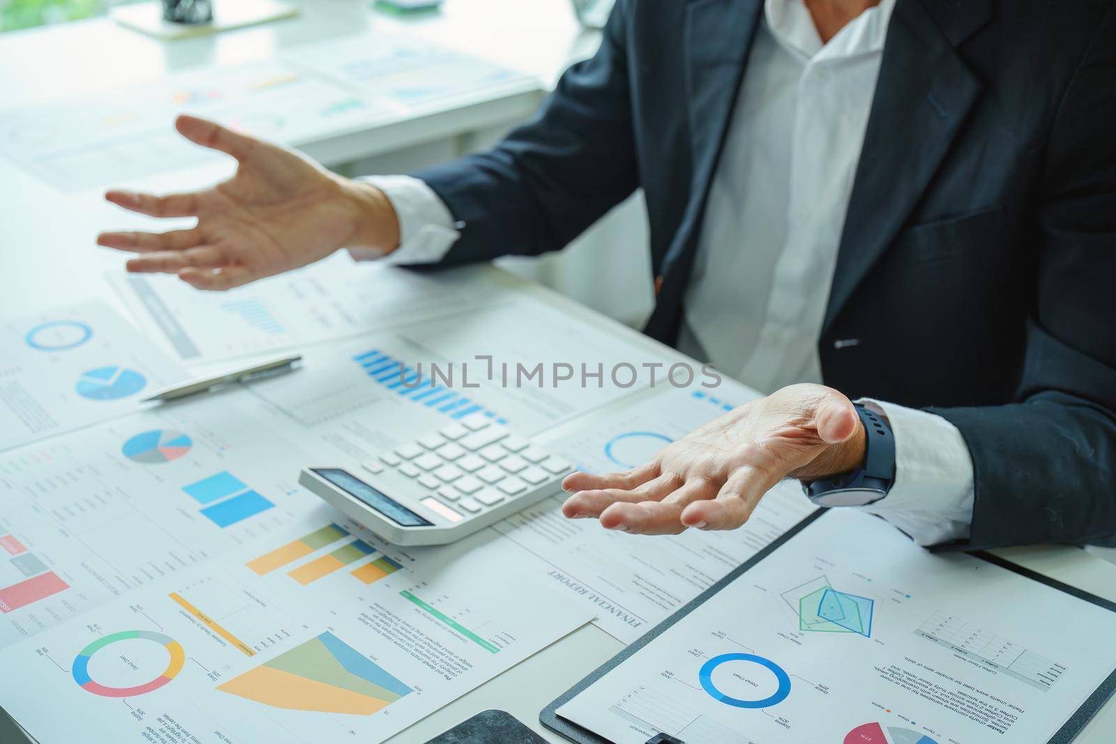 A male businessman or marketer gestures to explain an action plan to increase profits to the audience using the financial and investment budget document with a calculator in the conference room.