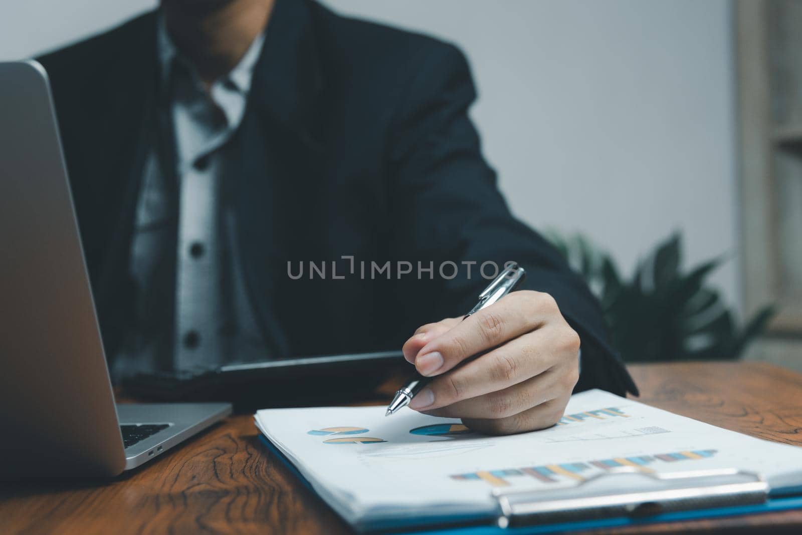 Businessman hand holding pen pointing paperwork chart report analysis statistic and document financial graph investment marketing on desk in company.