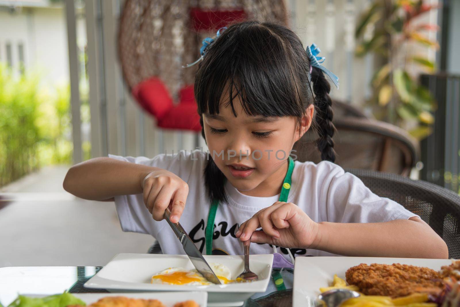 little girl asian eat fried egg on dish at table.