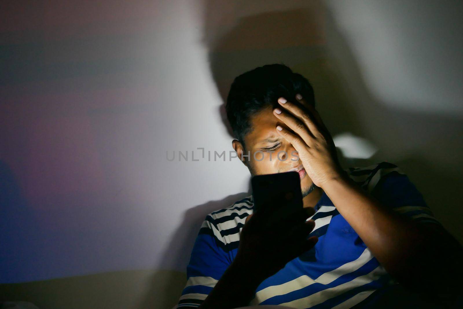 young man sitting on bed using smart phone at night .