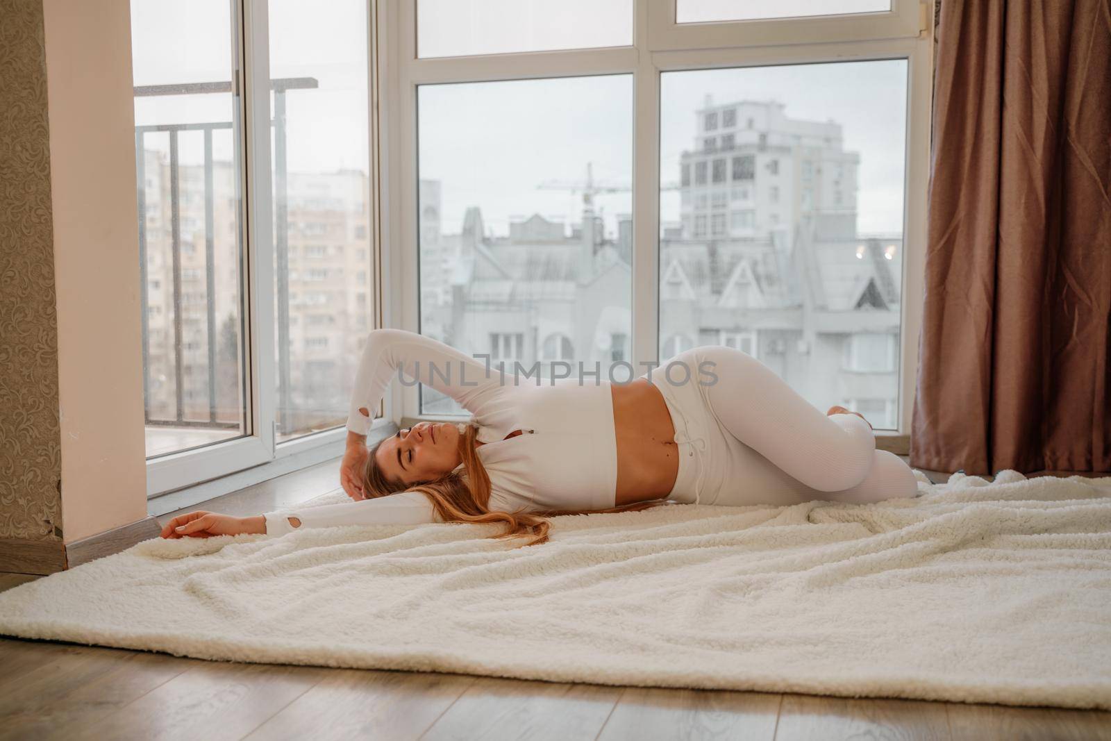 Side view portrait of relaxed woman listening to music with headphones lying on carpet at home. She is dressed in a white tracksuit. by Matiunina