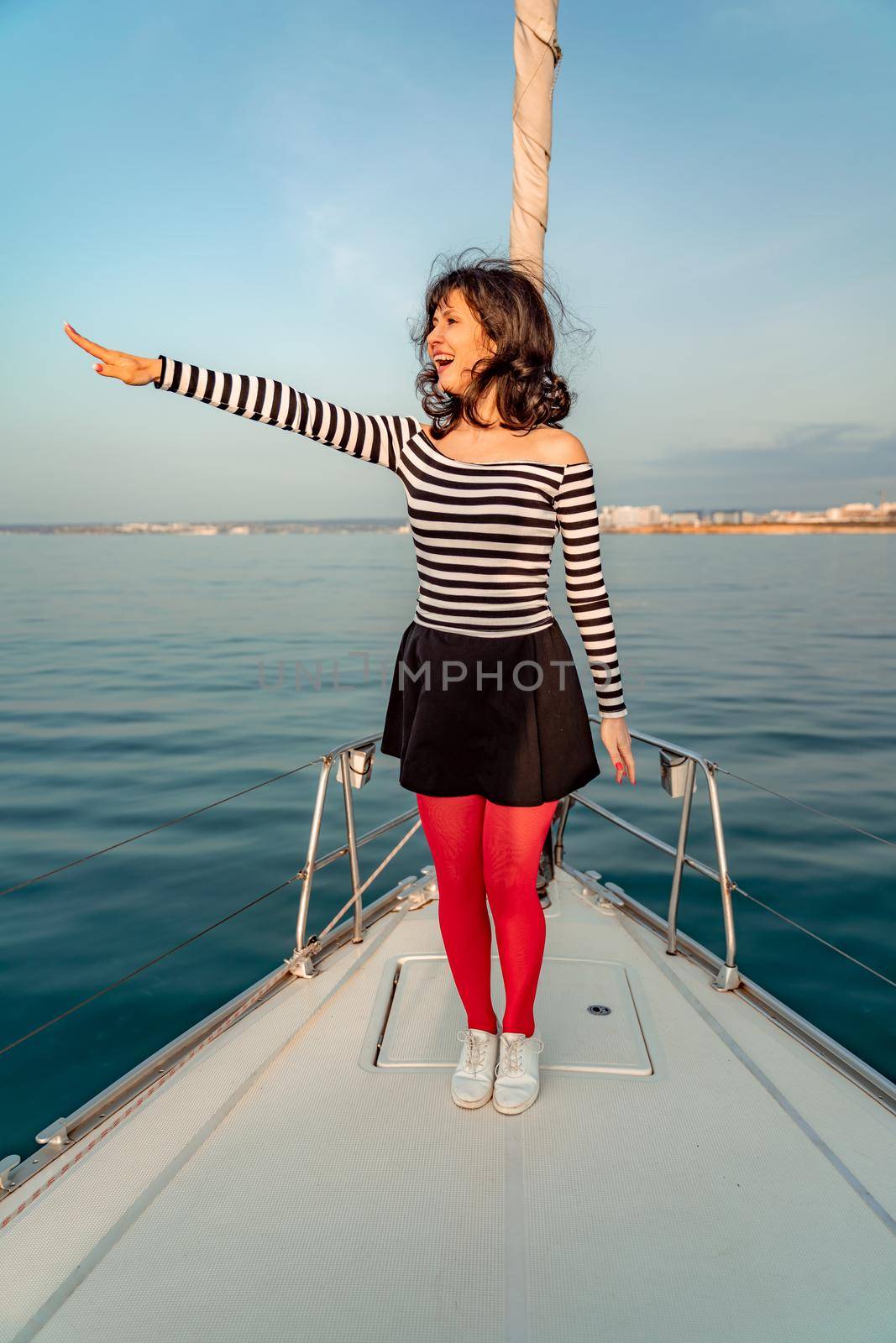 Woman standing on the nose of the yacht at a sunny summer day, breeze developing hair, beautiful sea on background by Matiunina