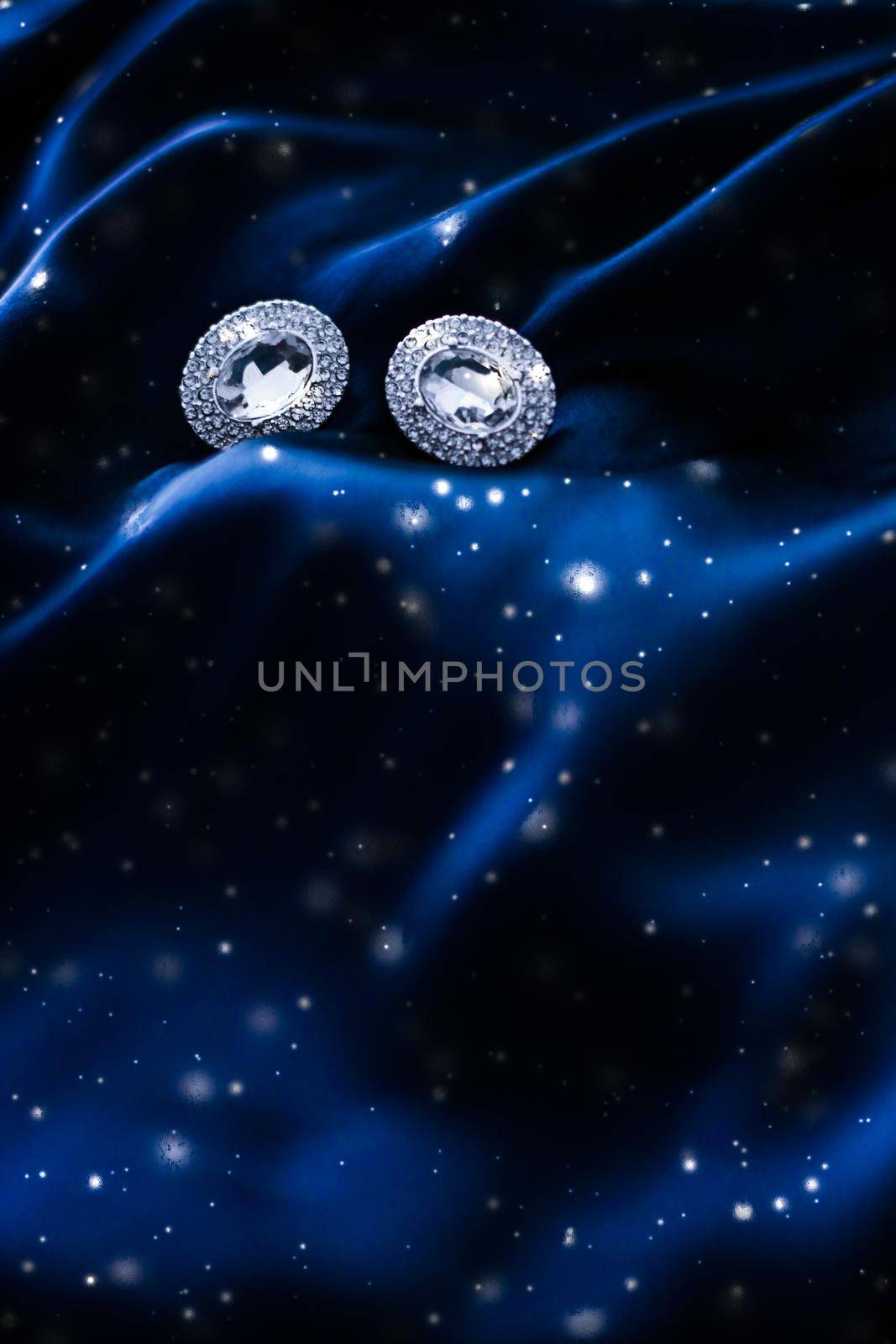 Jewellery brand, Christmas shopping and New Years gift concept - Luxury diamond earrings on dark blue silk with snow glitter, holiday winter magic jewelery present