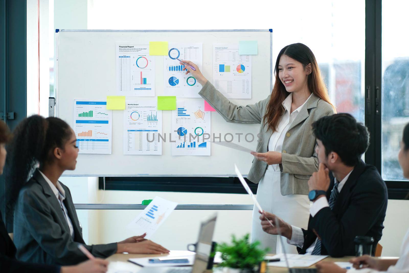 Female Operations Manager Holds Meeting Presentation for a Team of Economists. Asian Woman Uses Digital Whiteboard with Growth Analysis, Charts, Statistics and Data. People Work in Business Office. by wichayada