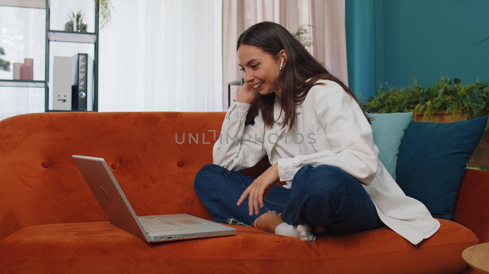 Portrait of caucasian girl sitting on couch, looking at camera, making video webcam conference call with friends or family, enjoying pleasant conversation. Young woman laughing, waving hello at home