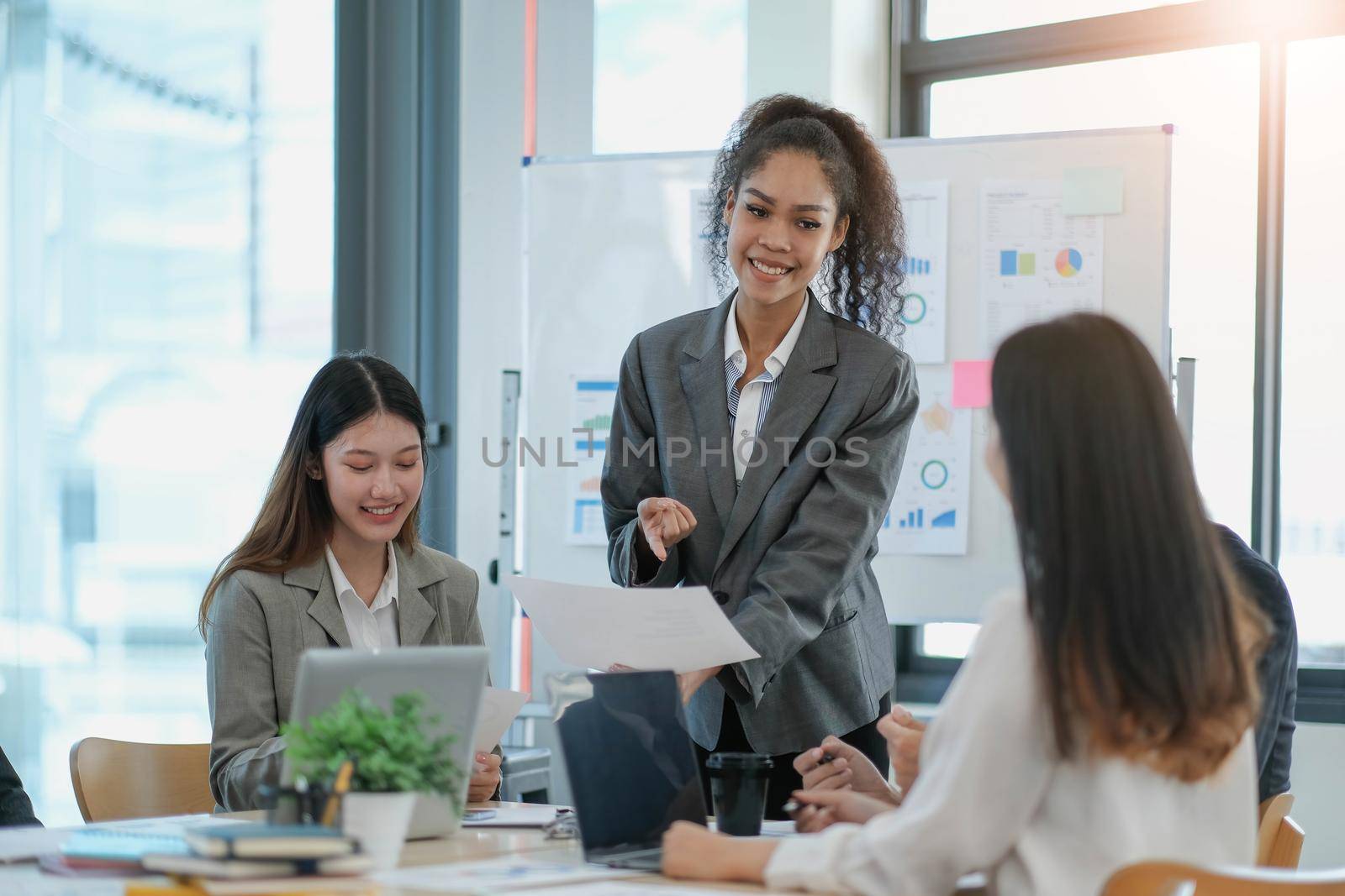 Asian business woman leader in a meeting with her multi-ethnic colleagues at the office presenting sales data or forecast for a project.