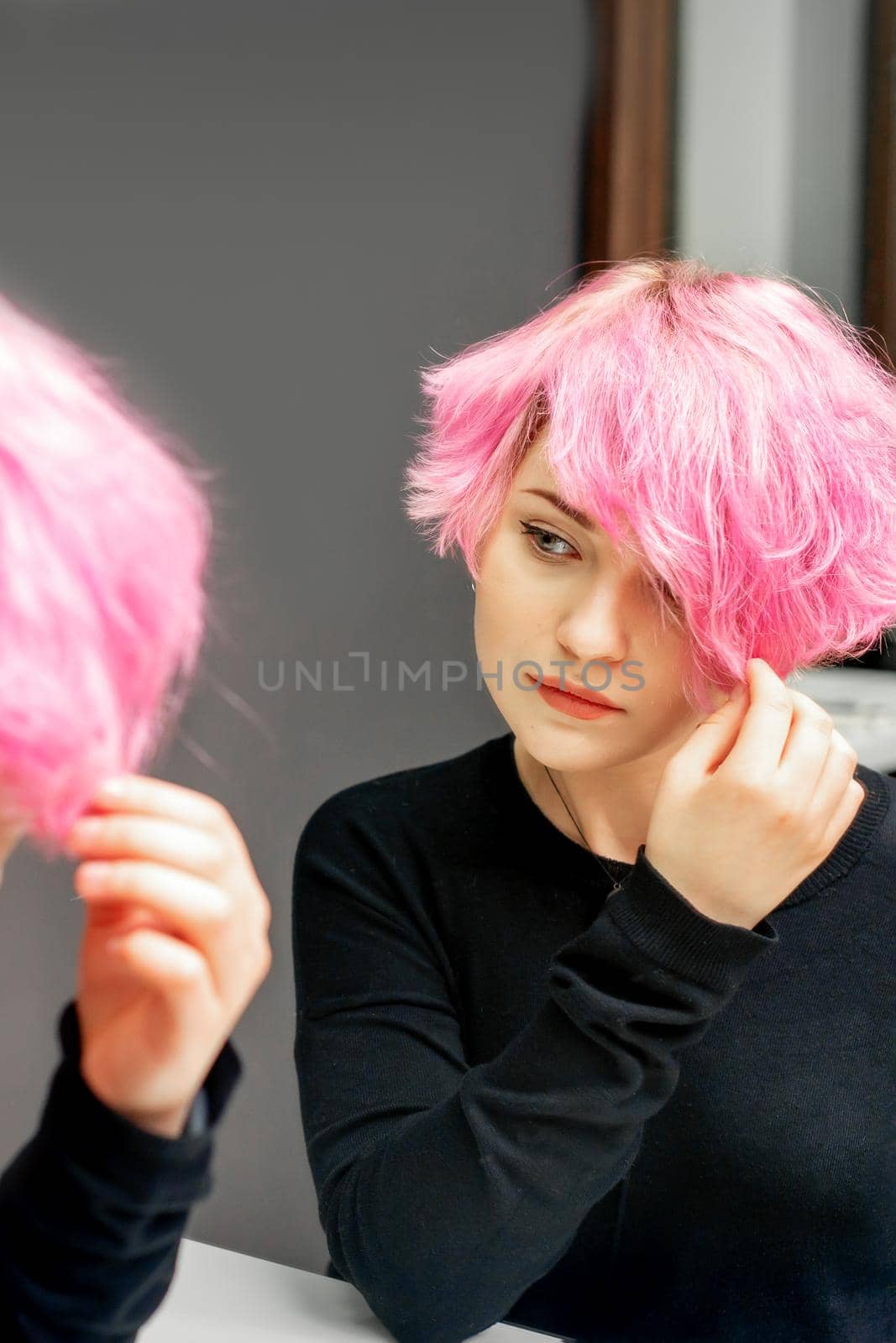 Beautiful young caucasian woman looking at her short pink hair in a mirror
