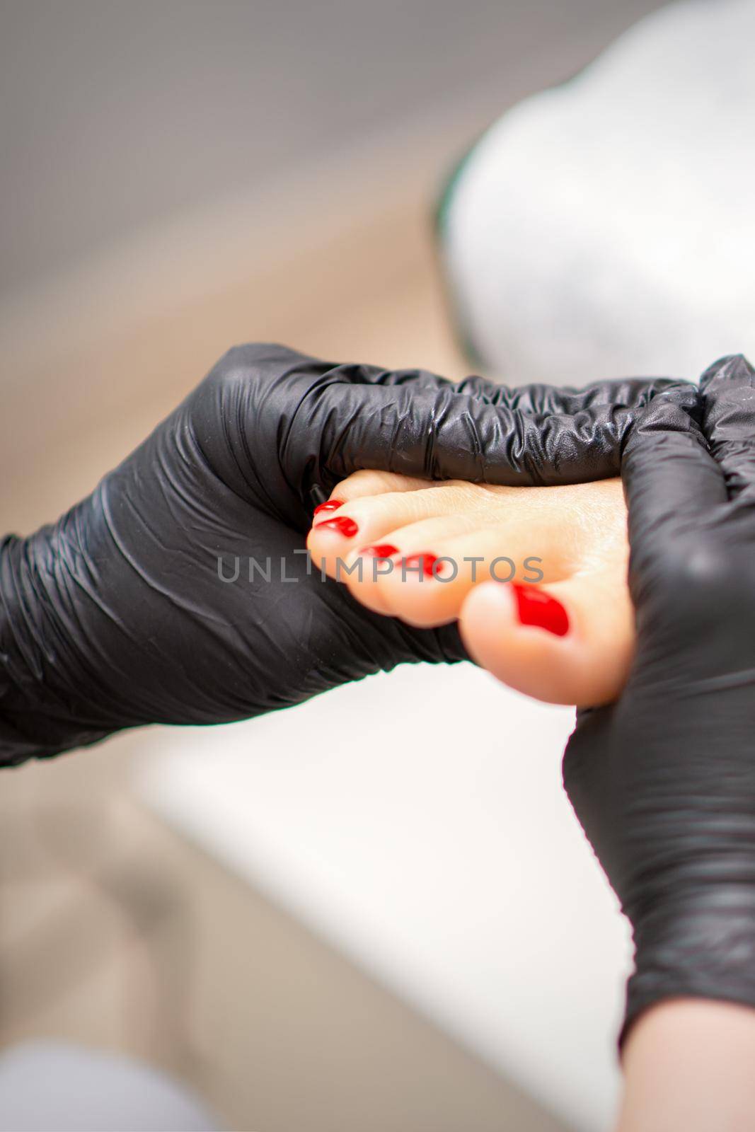 Foot massage with moisturizing and peeling cream by pedicurist hands wearing black gloves, close up. by okskukuruza