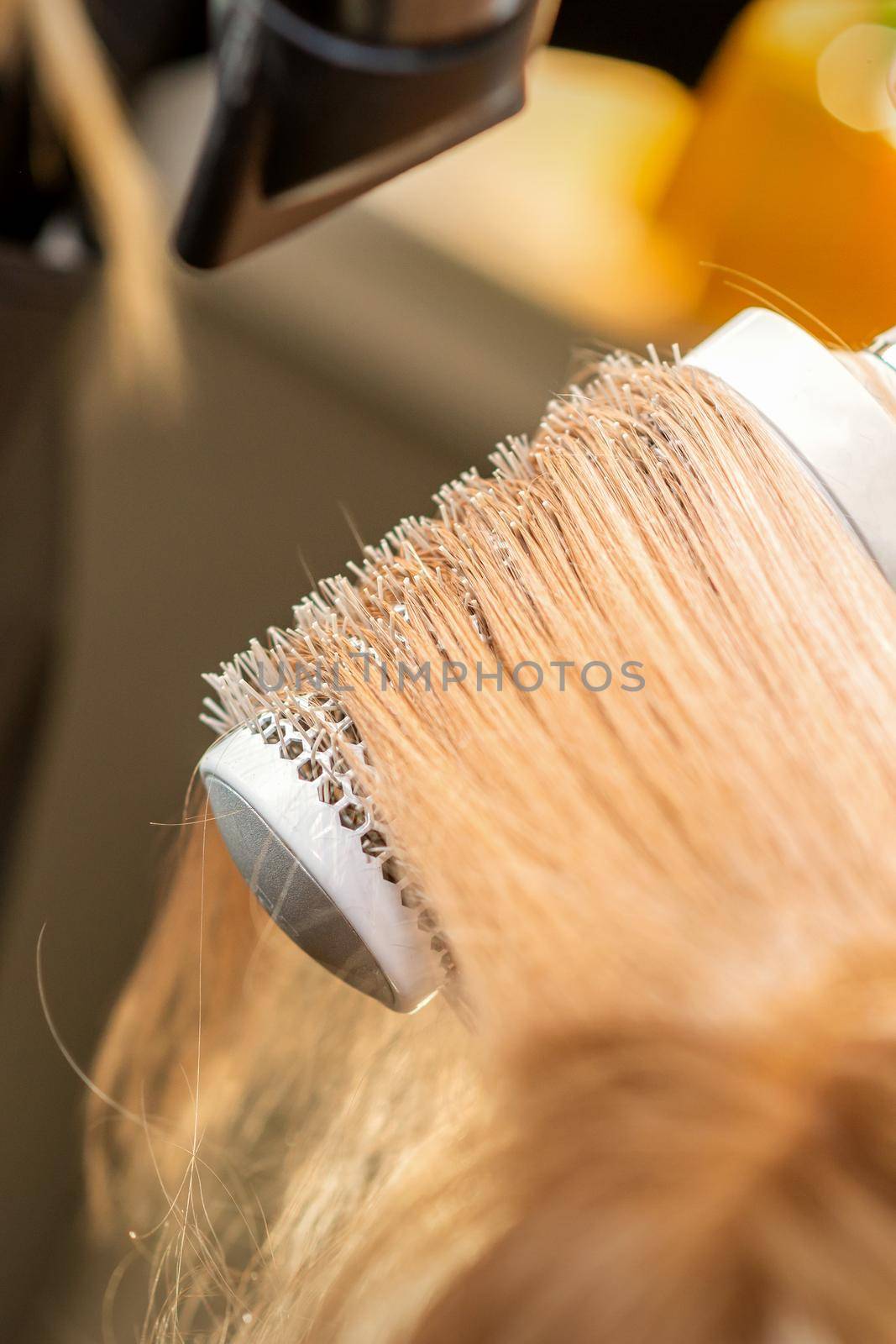 Hairdresser hand drying blond hair with a hairdryer and round brush in a beauty salon. by okskukuruza