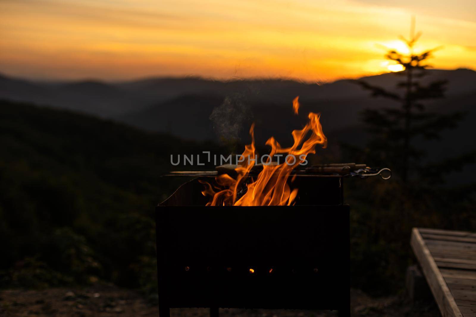 Burning wood at night. Campfire at touristic camp at nature in mountains. Flame amd fire sparks on dark abstract background. Cooking barbecue outdoor. Hellish fire element. Fuel, power and energy