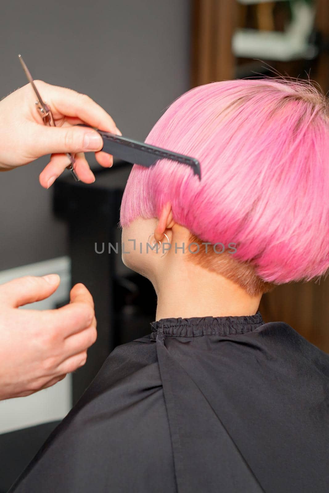 Hands of hairdresser combing hair making short pink hairstyle for a young caucasian woman in a beauty salon. by okskukuruza