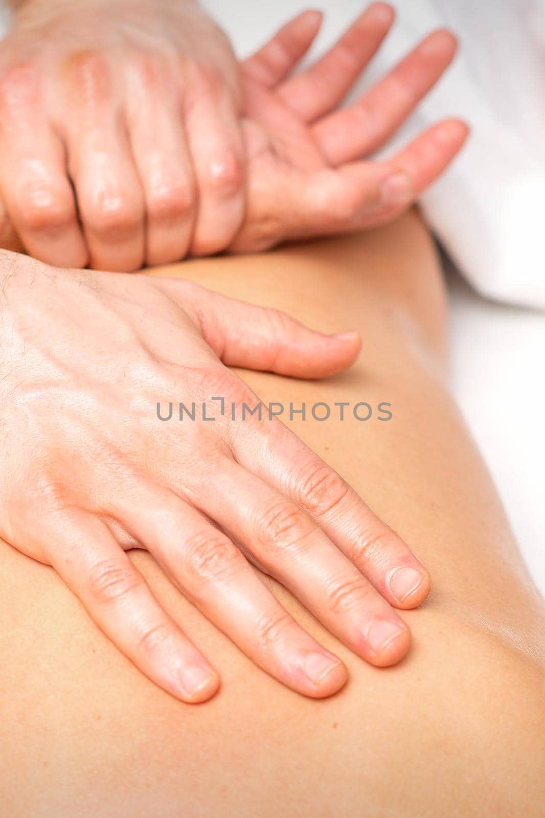 A male physiotherapist stretches the arms on the back of a man lying down, close up